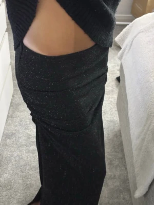 Svart glittrig långkjol - Säljer en svart långkjol med glittriga detaljer. Kjolen har en åtsittande passform och är gjord i ett stretchigt material som ger en snygg siluett. Passar mig på längden som är 165