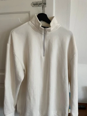 Vit hoodie med half zip och hög krage - Klassisk vit hoodie med hög krage och half zip-dragkedja framtill. Långärmad modell i mjukt material, perfekt för en avslappnad och stilren look. Enkel och clean design utan tryck eller mönster.