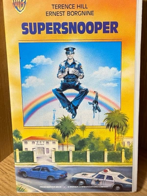 Supersnooper VHS-kassett - Supersnooper är en klassisk VHS-kassett med färgstark omslagsdesign. Filmen har Terence Hill och Ernest Borgnine i huvudrollerna och omslaget visar en tecknad polis framför en regnbåge och palmer. Kassetten är från Warner Home Video och har svensk text.