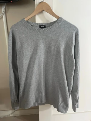 Grå basic tröja från Uniqlo - En stilren grå tröja från Uniqlo i storlek M. Tröjan har rund halsringning, långa ärmar och är tillverkad i ett mjukt, tunt material som passar perfekt till lager på lager. Enkel och clean design utan tryck eller mönster.