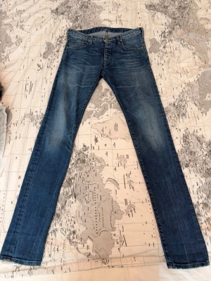 Blå slim fit jeans från Armani - Snygga blå slim fit jeans från Armani med klassisk femficksmodell och guldfärgade sömmar. Bakfickan har det ikoniska Armani-logotypen broderad. Jeansen är i ett mjukt denimtyg med lätt slitna detaljer för en avslappnad look.