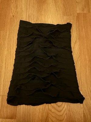 Svart tubtop med volang - Snygg svart kort klänning med volangdetaljer i lager på lager. Klänningen är axelbandslös och har en tight passform som framhäver figuren. Perfekt för dig som vill ha en stilren men ändå trendig look.Om du intreserad jag vill bara förvarana att dom här byxorna är från en liten företag som hetter jennifer.