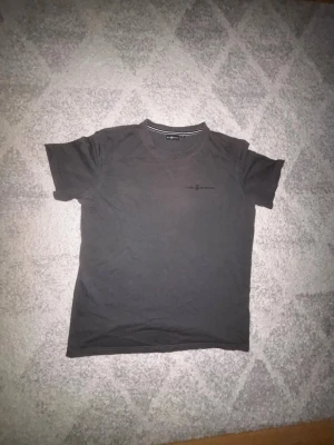 Mörkgrå t-shirt från Sail Racing - En stilren mörkgrå t-shirt från Sail Racing med diskret logga på bröstet. Klassisk rund halsringning och korta ärmar. Perfekt basplagg till garderoben och tillverkad i mjuk bomull för skön känsla. Priset är ej hugget i sten.