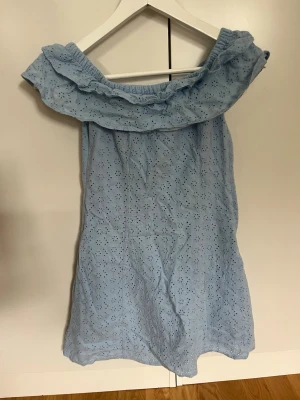 Ljusblå offshoulder klänning  - Söt ljusblå offshoulder klänning med volang upptill och broderade blommor i tyget. Den har även en dragkedja på sidan. Säljer då den var för liten för mig. Skulle säga att den är mer som storlek 34🥰