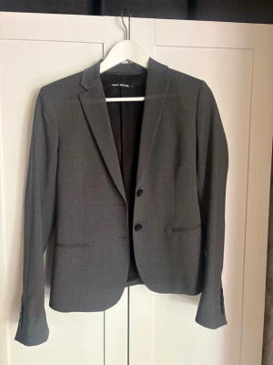 Mörkgrå kavaj från Filippa K - Mörkgrå kavaj från Filippa K med två knappar framtill. Kavajen har raka fickor och är helfodrad med svart innerfoder. 