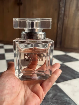 Karl Lagerfeld Eau de Parfum 85ml - Elegant parfym från Karl Lagerfeld i en stilren, transparent glasflaska med silverdetaljer och fyrkantigt lock. Flaskan har raka linjer och modern design, perfekt för dig som gillar exklusiva dofter och snygga flaskor på hyllan. Det fins 2/3 kvar. 