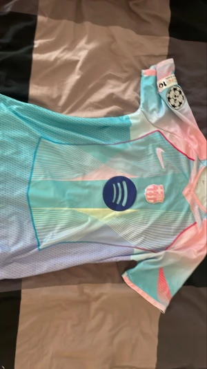 Barcelona matchtröja Lamine Yamal #10 - Snygg Barcelona matchtröja i ljusblått, rosa och vitt med tryck Lamine Yamal #10 på ryggen. Tröjan har Champions League-märke på ärmen, Nike-logga och Spotify som sponsor framtill. Tillverkad i lätt och ventilerande funktionsmaterial, perfekt för fotboll. 