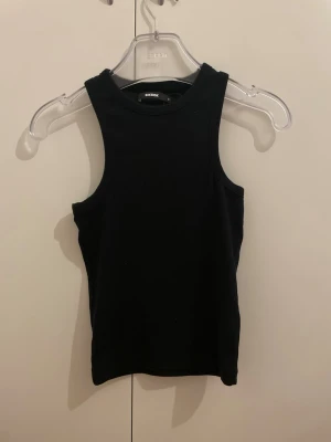 Svart ärmlös linnetopp från bikbok - Säljer en enkel och stilren svart linnetopp bikbok. Toppen är ärmlös med rund halsringning och har en tight passform som sitter snyggt på kroppen. Perfekt att matcha med jeans eller kjol för en clean look.