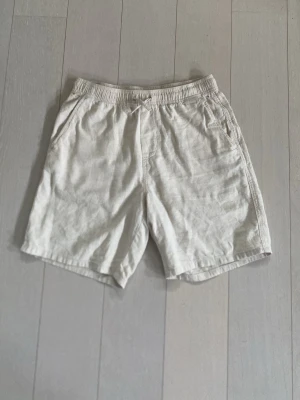 Linneshorts - Snygga och luftiga beiga shorts från H&M i linne. De har elastisk midja med snörning och två sidofickor. Perfekta för varma dagar och ger en avslappnad look.