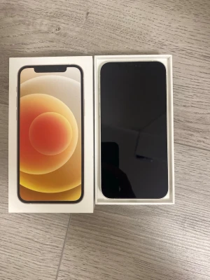 Vit iPhone 12 med originalkartong - Säljer en vit iPhone 12 från Apple. Telefonen har en stilren design med platt skärm, två kameror på baksidan och glasbaksida. Kommer i originalkartong. Dock kan ljudet gå ibland endast vid längre samtal annars är telefonen prima prima prima. 