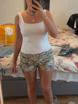 Camo shorts med låg midja - Säljer ett par snygga camouflage-mönstrade shorts i beige och gröna toner. De har låg midja, knapp och dragkedja framtill samt fickor på sidorna. Perfekta för sommaren och riktigt trendiga till ett enkelt linne eller crop top. Helt nya har aldrig använt