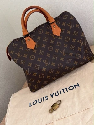 Vintage lv Monogram väska - Har kvitto för den, Klassisk Louis Vuitton Speedy handväska i brunt monogram canvas med ljusbruna läderhandtag och detaljer. Väskan har guldiga metalldetaljer och levereras med original dustbag och lås. Perfekt för dig som gillar lyxiga accessoarer och tidlös design.