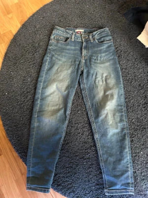 Blå jeans från Tommy Hilfiger - Snygga blå jeans från Tommy Hilfiger med klassisk femficksmodell och raka ben. Jeansen har en lätt tvättad look och detaljer med märkets logga på knapp och etikett. Perfekta för en avslappnad och trendig stil.