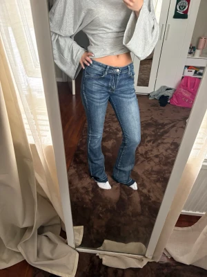 Blå bootcut jeans med kontrastsömmar - Snygga blå bootcut jeans med kontrastsömmar och klassiska fem fickor. Jeansen har låg midja och slitningar framtill för en trendig look. Perfekta för dig som gillar en avslappnad men ändå stilsäker stil.
