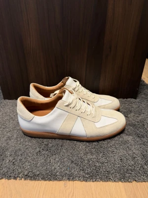 Vita sneakers Gats Skolyx - Snygga vita sneakers från Skolyx med beige mockadetaljer och klassisk gummisula. Skorna har en låg profil, vita skosnören och insida i ljust läder. Perfekta för dig som gillar stilrena och tidlösa sneakers. Box ingår!