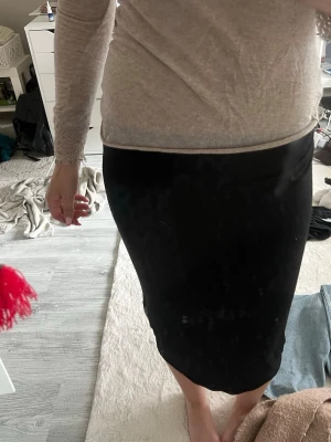 Svart långkjol i stretchigt material - En enkel och stilren svart långkjol med tight passform. Kjolen är rak i modellen och har en mjuk, stretchig känsla som gör den bekväm att bära. Perfekt att matcha med olika toppar för en clean look.