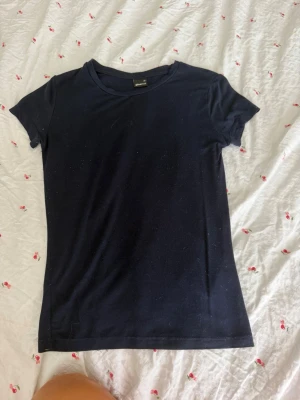 Mörkblå t-shirt från Gina Tricot - En enkel och stilren mörkblå t-shirt från Gina Tricot. Modellen har rund halsringning och korta ärmar. Perfekt basplagg som passar till allt och är gjord i mjuk bomull för skön känsla hela dagen.
