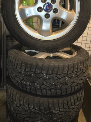 Saab vinterdäck dubbade 16 tum - Säljer fyra dubbdäck med silverfärgade aluminiumfälgar från Saab. Däckens mönsterdjup och dubbar syns tydligt, perfekta för vinterväglag. Passar till bil och ger bra grepp på is och snö.