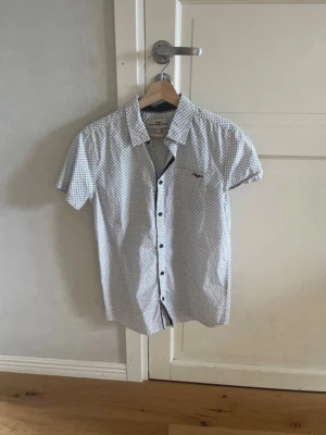 Hampton Republic skjorta - Vit skjorta med blå detaljer i gott skick. Dock en fläck på vänster axel (se bild 2), men inget jag upplever syns när man använder den. Bara att höra av dig vid funderingar/prisförslag.
