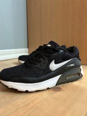 Nike Air Max 90 svart/vit sneaker - Nike Air Max 90 sneakers i svart mesh och syntet med vit sula och vit swoosh. Klassisk Air Max-dämpning i hälen och svarta skosnören. Tidlös modell som passar till det mesta och har en sportig vibe.
