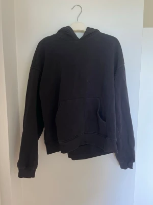 Svart hoodie med ficka - En svart hoodie med en ficka framtill och huva. Hoodien har långa ärmar och ribbade muddar vid ärmslut och nederkant. Perfekt för en avslappnad och chill stil. Materialet känns mjukt och bekvämt.