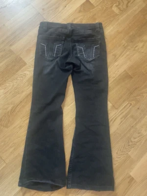 Svarta lågmidjade jeans från Gina Tricot - Säljer ett par svarta bootcut jeans med vita kontrastsömmar på bakfickorna. Jeansen har klassisk femficksdesign och utsvängda ben. Perfekta för dig som gillar en retroinspirerad look.