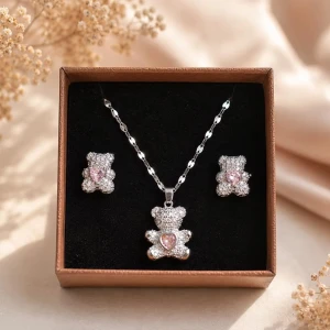 Teddy Love Smyckeset  - Setet består av ett halsband och matchande örhängen, perfekta både till vardag och speciella tillfällen. Material: Rostfritt stål ( S.Steel Stämplat ), Örhängesstift i  silver 925 Storlek: Örhängen  ca 1.5 cm hög och 1,3 cm bred Halsband: längd ca 22–25 cm ( justerbar ) , Berlock 2 cm hög och 1,5 cm bred 🎁 Asken ingår.
