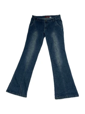 Blå bootcut jeans med utsvängda ben - Blå bootcut jeans med utsvängda ben och klassisk femficksdesign. Jeansen har en markerad söm-detalj framtill och baktill längs benen. Mjuka och elastiska. Midjemått: 33 tum, Innebenslängd: 33 tum. Lågmidjade. 