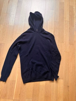 Mörkblå Kashmir hoodie  - En stilren kashmir hoodie med huva och långa ärmar. Hoodien är tillverkad i ett mjukt, tunt material som känns skönt mot huden. Passar perfekt för en avslappnad look och är enkel att matcha med andra plagg. (Oscar Jacobson)