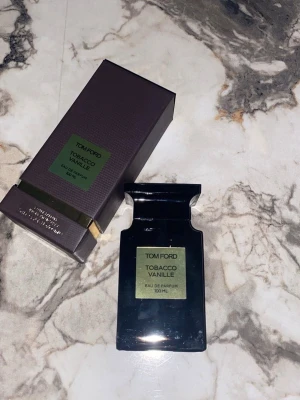 Tom Ford Tobacco Vanille EdP 100ml - Tom Ford Tobacco Vanille Eau de Parfum i en lyxig svart glasflaska med guldgrön etikett. Flaskan rymmer 100 ml och kommer i en elegant mörkbrun kartong med gulddetaljer. En ikonisk doft med inslag av tobak och vanilj.