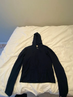 Svart hoodie med dragkedja - En stilren mörkblå hoodie med dragkedja framtill och huva med dragsko. Hoodien har långa ärmar och är tillverkad i ett mjukt tyg som passar perfekt för en avslappnad look. Enkel och klassisk design utan synliga loggor eller tryck.