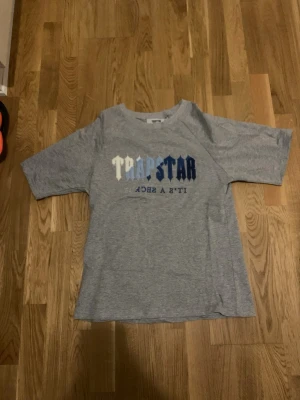 Äkta Trapstar It’s a Secret Kortärmad Tröja. - Säljer en grå t-shirt från Trapstar med stort broderat tryck i vitt, ljusblått och mörkblått på bröstet där det står 'TRAPSTAR' och 'IT'S A SECRET'. T-shirten har rund hals och raka, den är en small fit och då passar för storlek S ( Small ). Perfekt för en streetwear-look. Pris kan diskuteras vid rimliga priser.  Om du har frågor om varorna på min sida kan du skicka ett meddelande till detta konto.