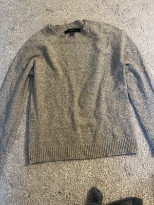 Beige/brun stickad tröja från Veromoda  - Klassisk beige/brun stickad tröja från Veromoda med rund halsringning och ribbade muddar vid ärmslut och nederkant. Tröjan har en rak passform och är tillverkad i ett mjukt, värmande material som passar perfekt för kyligare dagar.