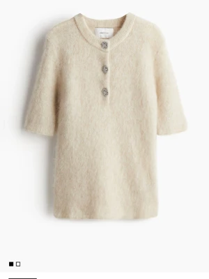 Ny Beige stickad topp tröja  med smyckesknappar hm Stl s - Säljer en fluffig, beige  stickad topp från  HM kort ärmar och rund hals. Toppen har tre dekorativa smyckesknappar framtill som ger en lyxig touch. Materialet ser ut att vara en mjuk ull- eller mohairblandning.