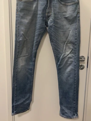 Blå slim fit jeans med slitningar - Snygga blå slim fit jeans med lätt slitna detaljer och tvättade partier på benen. Klassisk femficksmodell med normal midja och smal passform. Jeansen har kontrastsömmar och en modern look som passar till det mesta.