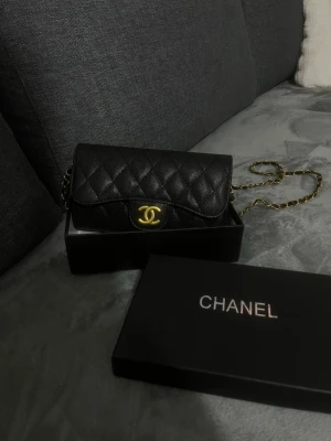  handväska - Snygg svart quiltad handväska från Chanel med klassiskt guldigt CC-spänne och kedjerem i guld och svart läder. Väskan har en tidlös design och är tillverkad i exklusivt läder med elegant struktur. Perfekt accessoar för att lyfta din outfit.