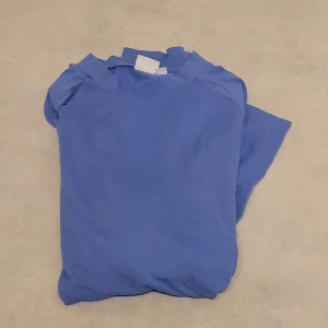 Blå långärmad funktionströja - En enkel blå långärmad tröja i mjukt material. Tröjan har rund halsringning och raka ärmar, perfekt för en avslappnad stil. Passar bra till jeans eller under en jacka. Inga synliga loggor eller mönster.