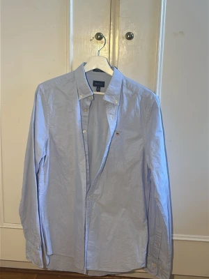 Ljusblå skjorta från Gant - Klassisk ljusblå skjorta från Gant med button-down krage och broderad logga på bröstet. Skjortan har långa ärmar, knappar framtill och är tillverkad i mjuk bomull. Perfekt för en clean och stilren look.