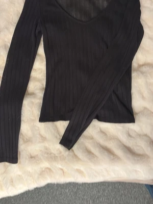 Svart ribbad topp från Nelly - Snygg svart ribbad topp från Nelly med lång ärm och v-ringad hals. Toppen är croppad och har en tight passform som framhäver figuren. Perfekt att styla med höga jeans eller kjol för en trendig look.