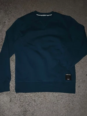 Mörkblå sweatshirt från Björn Borg - Mörkblå sweatshirt från Björn Borg med rund halsringning och ribbade muddar. Tröjan har en svart patch med logga nertill och är tillverkad i mjukt material, perfekt för en chill och stilren look.