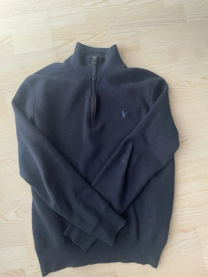 Mörkblå halvzip från Polo Ralph Lauren - Mörkblå stickad tröja från Polo Ralph Lauren med halv dragkedja och hög krage. STORLEKEN ÄR S MEN SITTER SOM XS. Materialet är mjukt och passar perfekt för lager på lager.