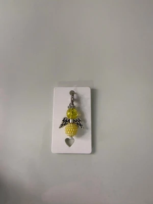 Gul ängelberlock med pärlor - Unik berlock formad som en ängel med gula pärlor och silvriga vingar. Perfekt att hänga på ett halsband, armband eller väska. Gjord av metall och plastpärlor i en cool design som sticker ut.