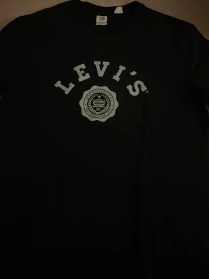 Svart Levi's långarmad med logga - Snygg svart långarmad  från Levi's med klassisk logga och emblem tryckt på bröstet. T-shirten har rund hals och korta ärmar, perfekt för en avslappnad och stilren look. Tillverkad i mjuk bomull för skön komfort.