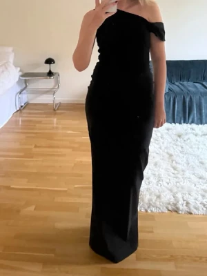 Svart oneshoulder långklänning - Elegant svart långklänning med oneshoulder-design. Klänningen har en smickrande, figurnära passform och är perfekt för speciella tillfällen. Tidlös och stilren look som ger en lyxig känsla. Använd 1 gång 