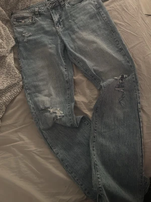 Blå slitna jeans från Nelly  - Säljer ett par blå jeans från Nelly  med slitningar och hål på låret och knät. Jeansen har en klassisk femficksmodell, raka ben och är tillverkade i bomull. Perfekta för en avslappnad och trendig look. Ordninarie pris är 1200 och är aldrig använda 