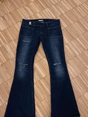Mörkblå bootcut jeans med slitningar - Säljer ett par mörkblå bootcut jeans med slitningar vid knäna och lätt tvättade detaljer. Jeansen har framfickor och bakfickor är low waist bootcut. Köpta från Gina Tricot 14+ i storlek M och är endast använda dn gång. Pris kan diskuteras 