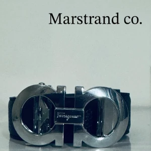 Svart skärp med silverdetalj Ferragamo - Snyggt svart skärp från Salvatore Ferragamo med en stor, blank silverspänne i ikonisk dubbel Gancio-design. Perfekt accessoar för att lyfta vilken outfit som helst med en lyxig touch. Klassisk och tidlös look.