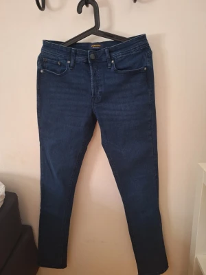 Mörkblå Jack & Jones 29/34 - Säljer ett par mörkblå skinny jeans med klassisk femficksdesign och hög midja. Jeansen har smal passform och är tillverkade i stretchigt denimtyg för extra komfort. Perfekta till en avslappnad eller trendig look.