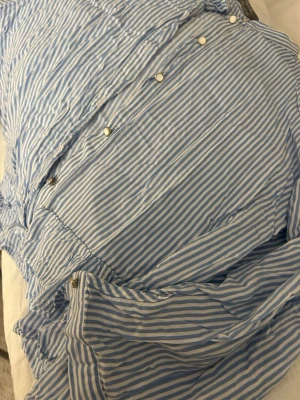 Blårandig blus med volanger - Snygg blus med blåvita smala ränder och dekorativa volanger i storlek L, men sitter som en S! Blusen har knappar framtill och är tillverkad i ett lätt, vävt material som känns luftigt. Perfekt till sommaren! Säljer då jag inte använder och denna går är inte tillgänglig att köpa i butik!💘