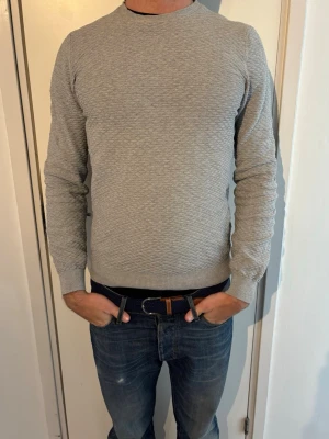 Massimo Dutti tröja   - Snygg grå tröja från Massimo Dutti i en mjuk mix av bomull och kashmir. Tröjan har rund halsringning, diskret strukturmönster och ribbade muddar vid ärmslut och nederkant. Perfekt för en stilren och enkel look.